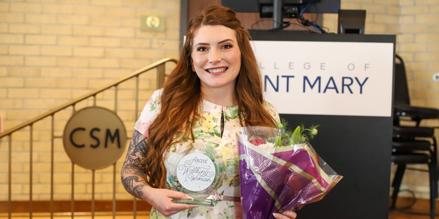 College of Saint Mary student Alexis Winter wears a floral dress and poses with a bouquet of flowers and her Heart of the Walking Woman award.