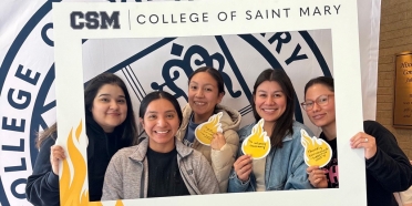 Five College of Saint Mary students pose in front of a step-and-repeat that features the College's seal.