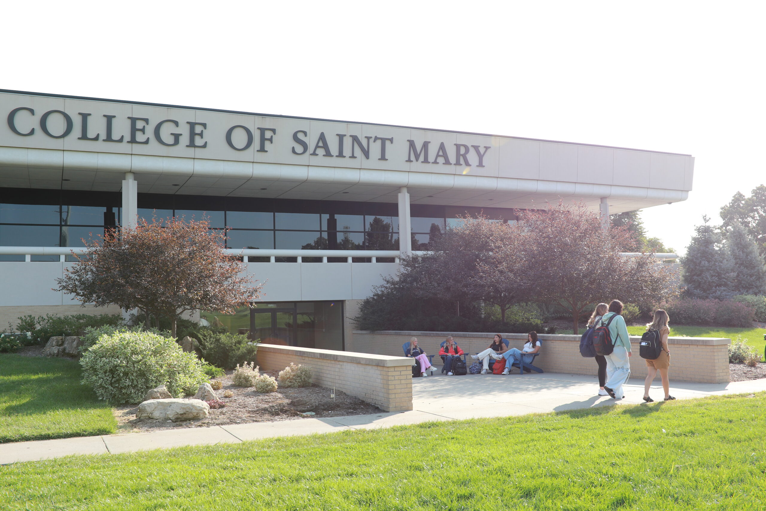 Students sit in front of and walk by Mercy Hall on campus.