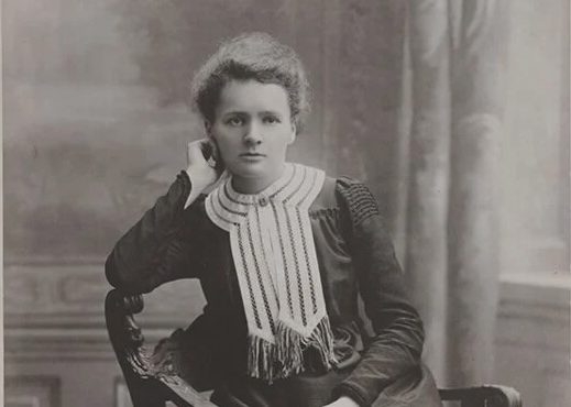 A young Marie Curie poses for a photo in chair.