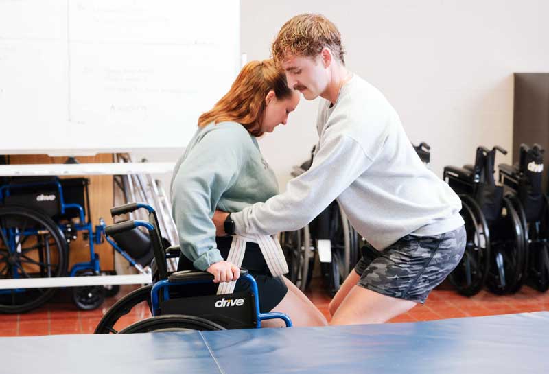 student helping another student out of a wheelchair