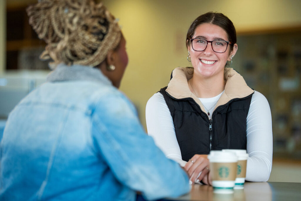 Smiling woman in conversation with Starbucks coffee cup at a table with another woman.
