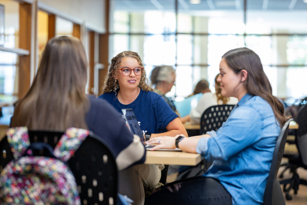 Students sitting at a table and talking in a bright campus study space.