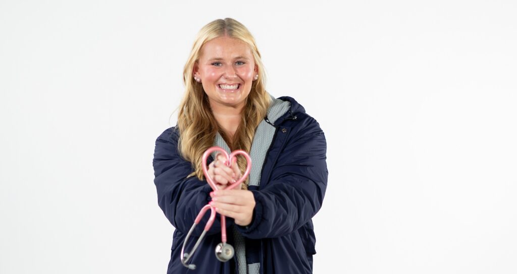 female swimmer holding a stethoscope, smiling at camera