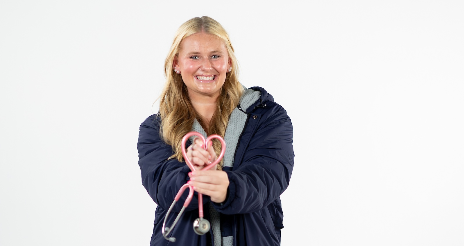 Nursing student and swimmer Kylee Brown stands in athletic attire with pink stethoscope in heart formation,