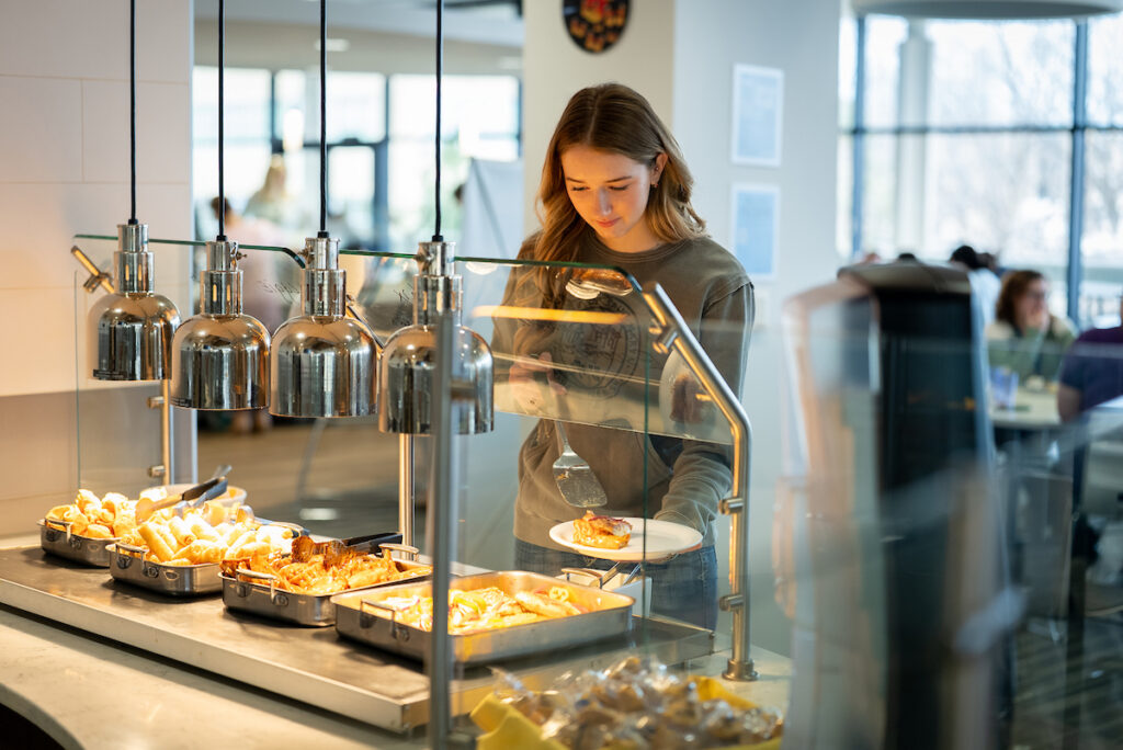 A student selecting food at a campus dining hall serving station.