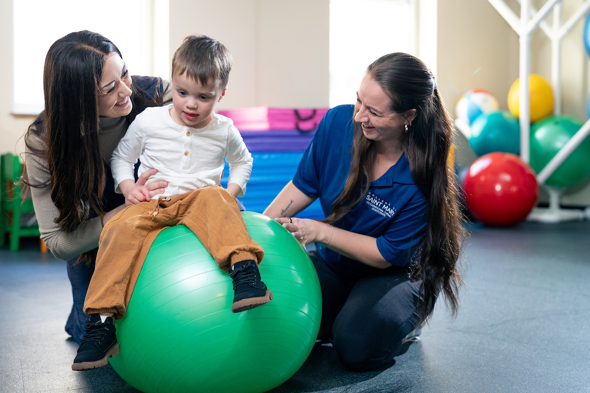 Occupational therapy student works with young child in pediatrics OT lab using a therapy ball.