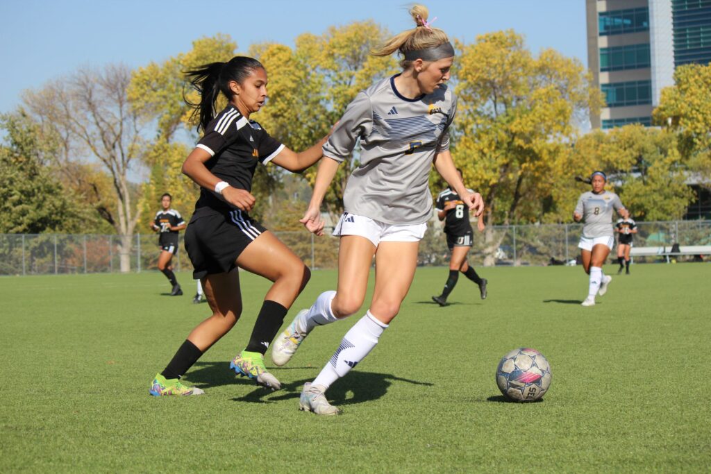 Students playing a soccer game on a campus athletic field during a recreational or intramural activity.