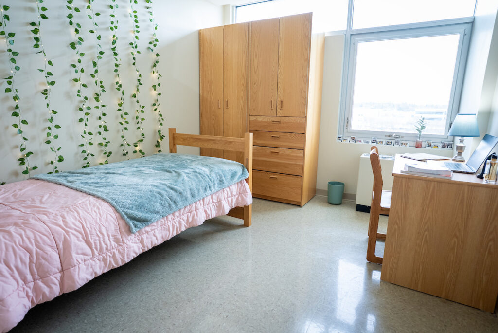 Single‑occupancy room in Stevens Hall featuring a bed, desk, dresser, wardrobe, and window with natural light.
