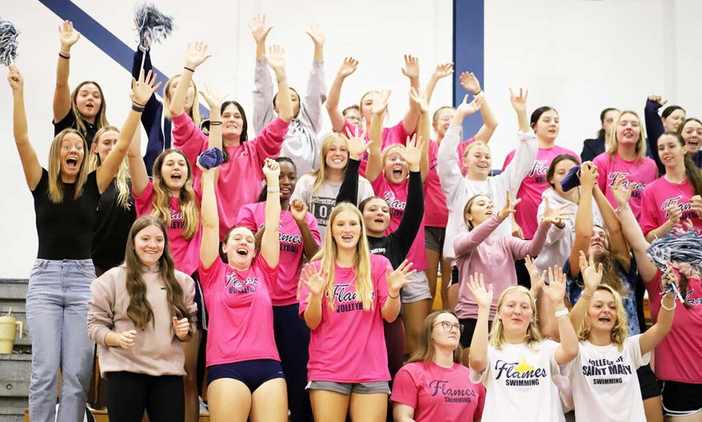 Students cheering and raising their arms together at a campus event, showing school spirit and community.