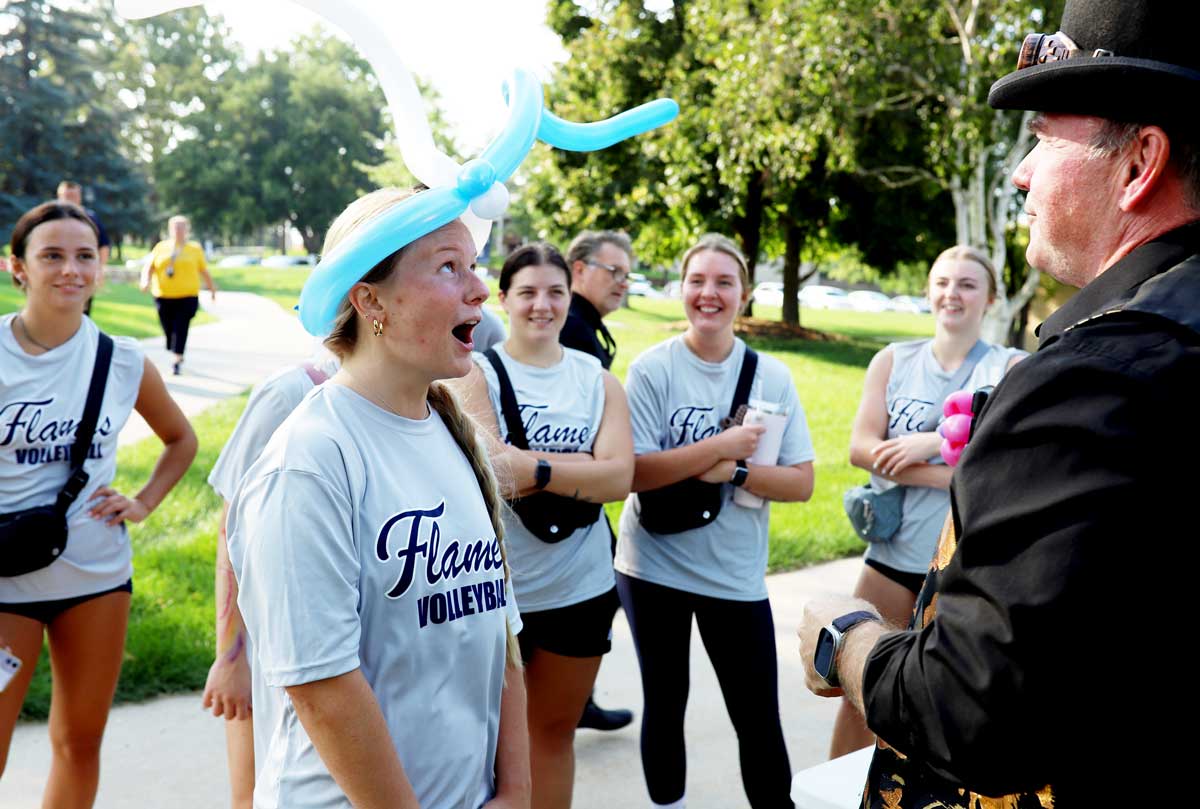 Students gather around friend who received a balloon animal hat at a campus event on the quad at College of Saint Mary.
