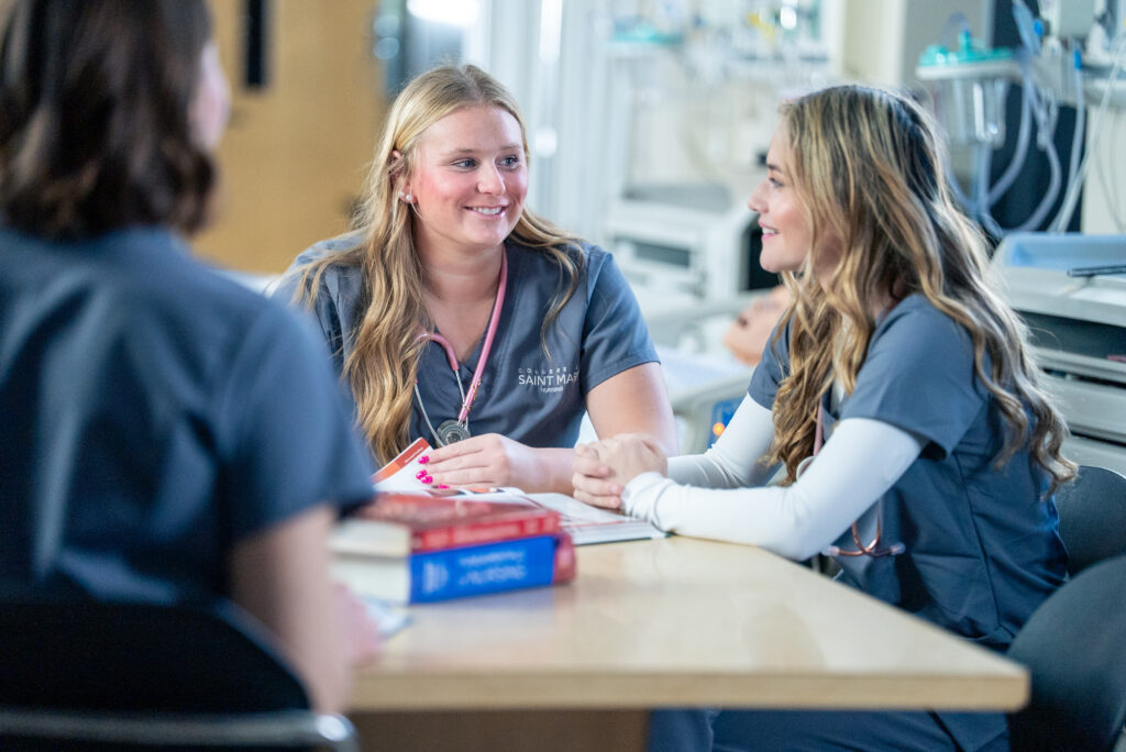 Three nursing students wearing grey scrubs study together.