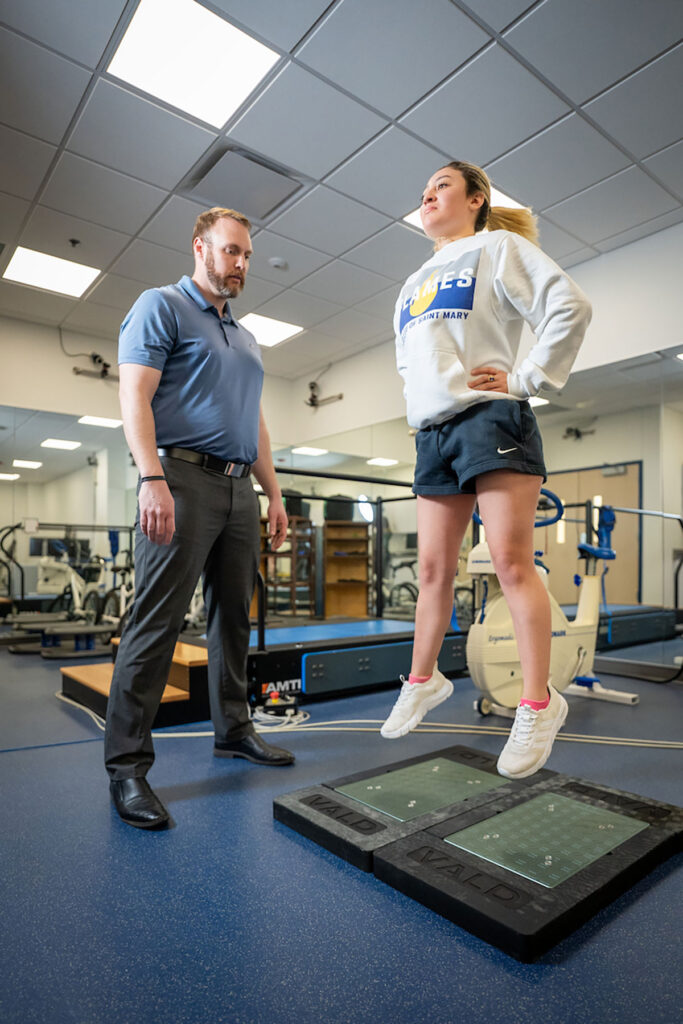 Instructor observes a student standing on balance platforms in kinesiology and exercise science lab.