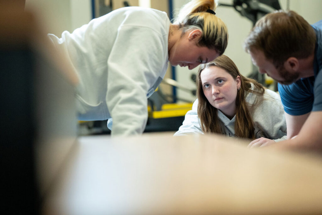 Students collaborate together with faculty member during a kinesiology exercise or rehabilitation lab session.
