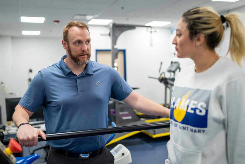 Student and instructor talk in a campus kinesiology exercise or rehabilitation lab.