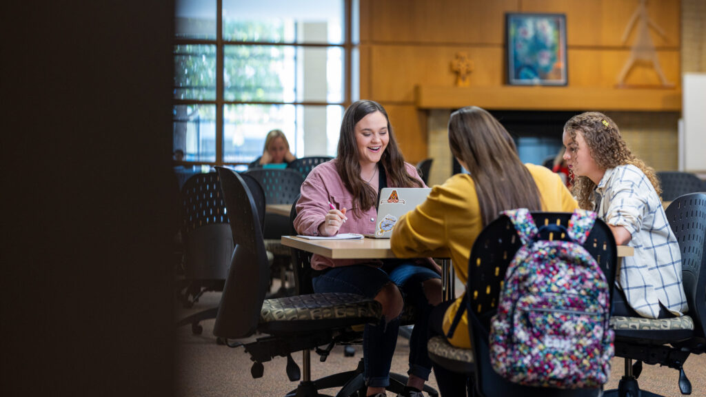 Three students studying together at a table in a campus library.