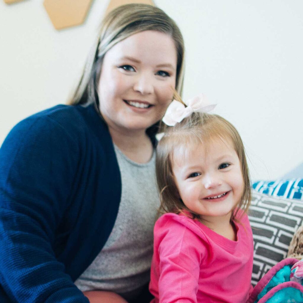 A mother in a blue blazer smiling with her daughter in a pink dress