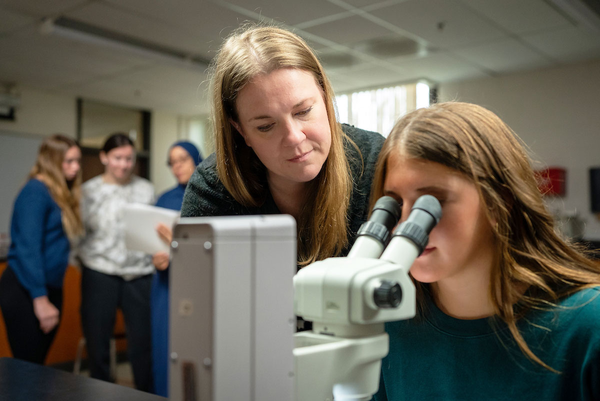 Instructor observing student in classroom lab who is looking into a microscope.