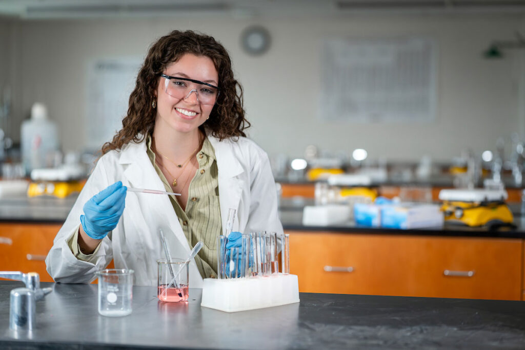 Female science student wearing a lab coat and gloves conducting an experiment in a school laboratory.