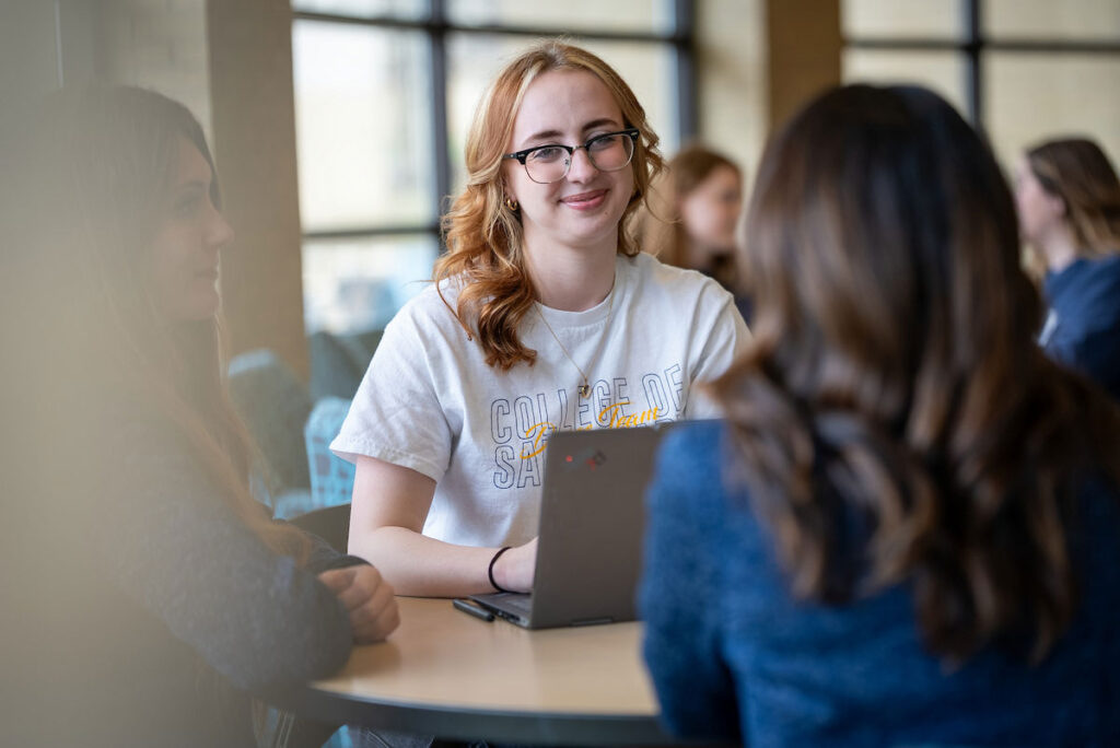 Students gather around a table with a laptop in Hixson-Lied Commons at College of Saint Mary.