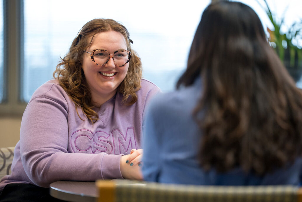 Student success advisor sits with student at table talking.