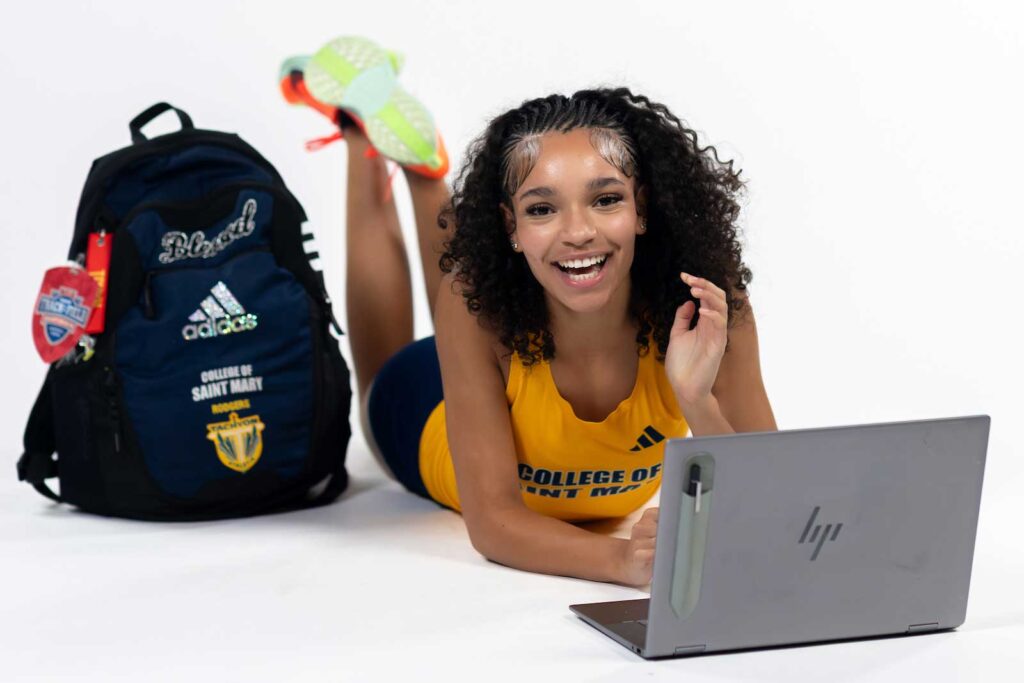 track athlete smiling at the camera while studying on a laptop
