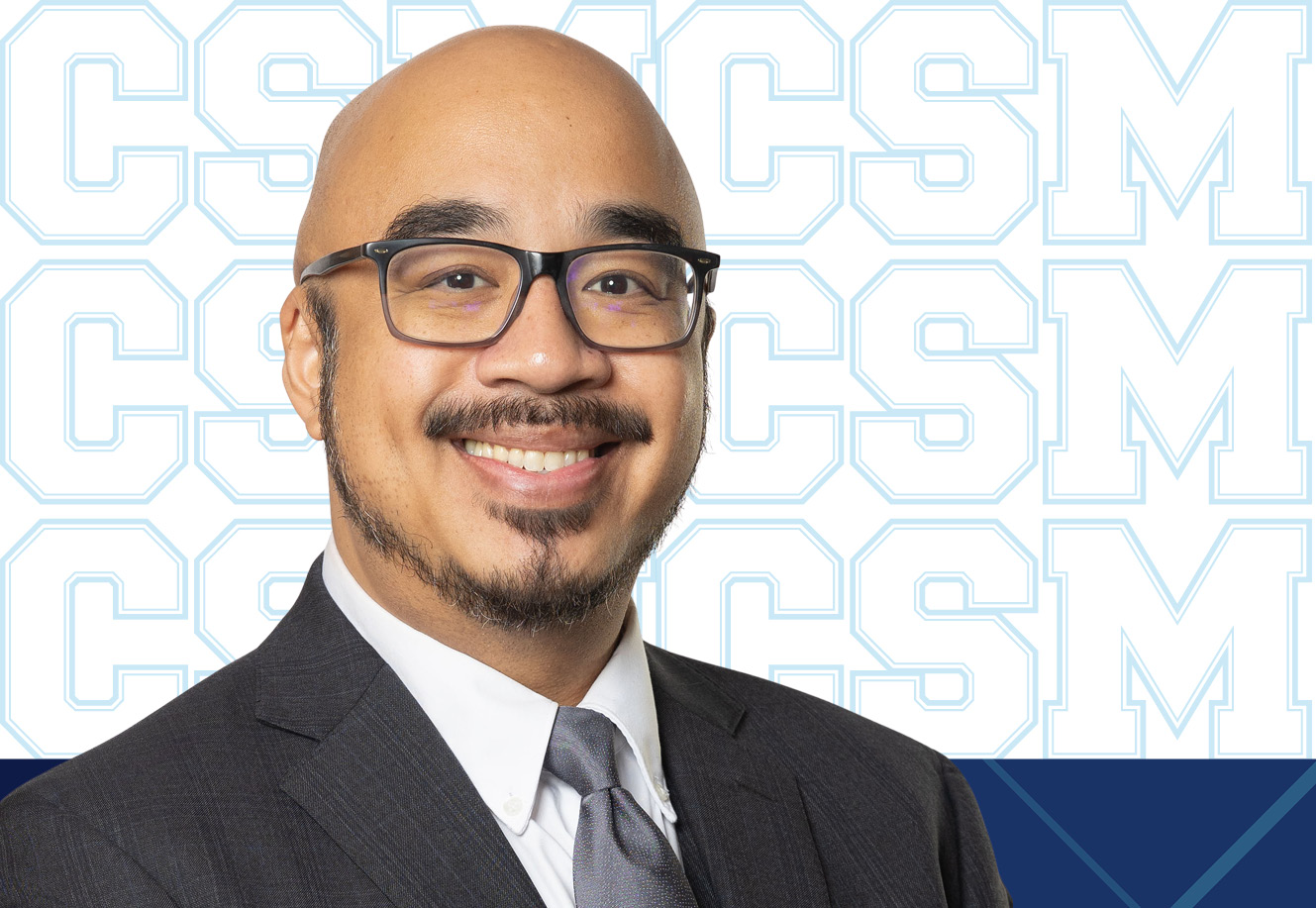 Master of Science in Organizational Leadership alum Sean Soliva wears a suit, tie and glasses. His image is in front of a CSM branded background.