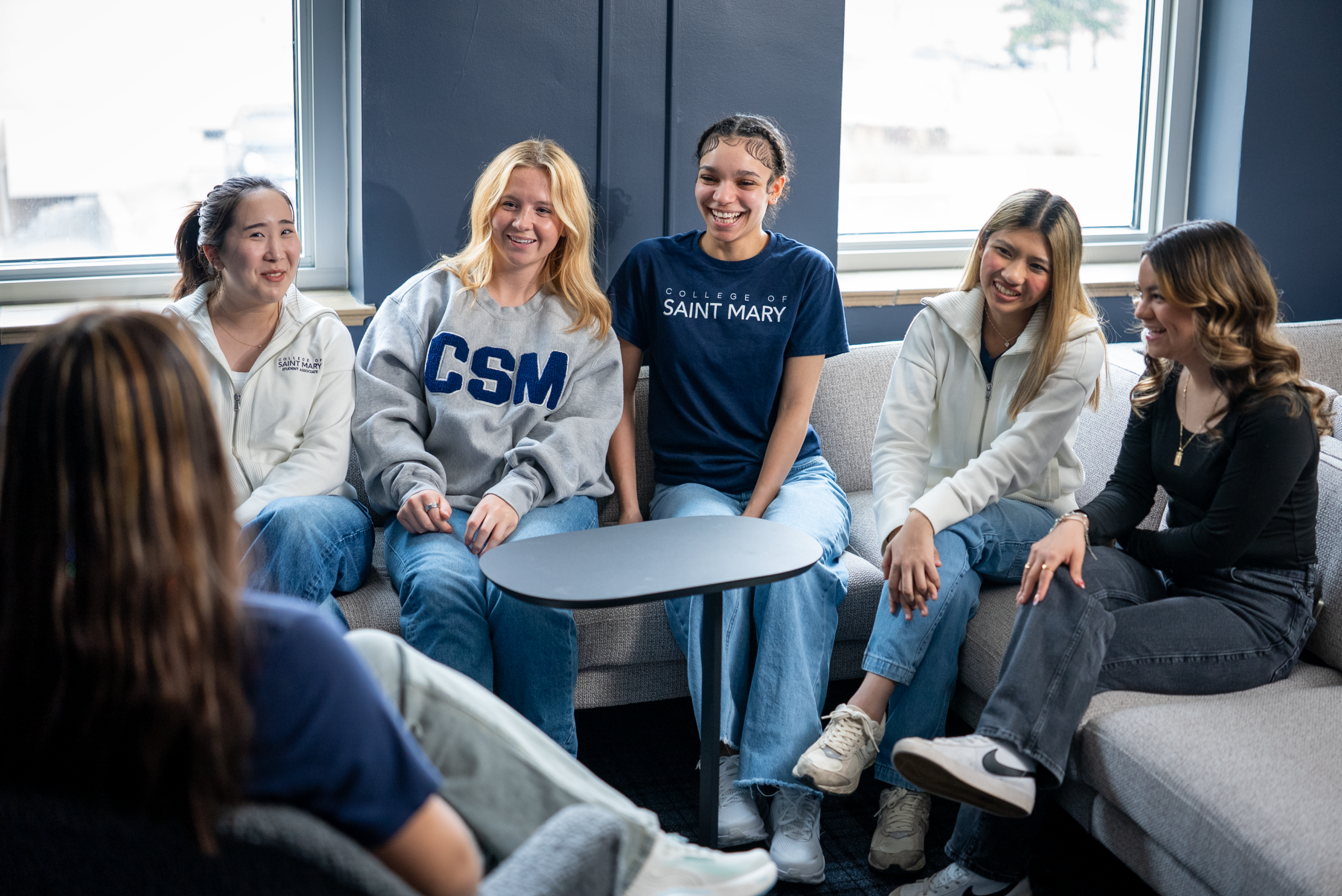 A group of students sit on a couch while talking and laughing.
